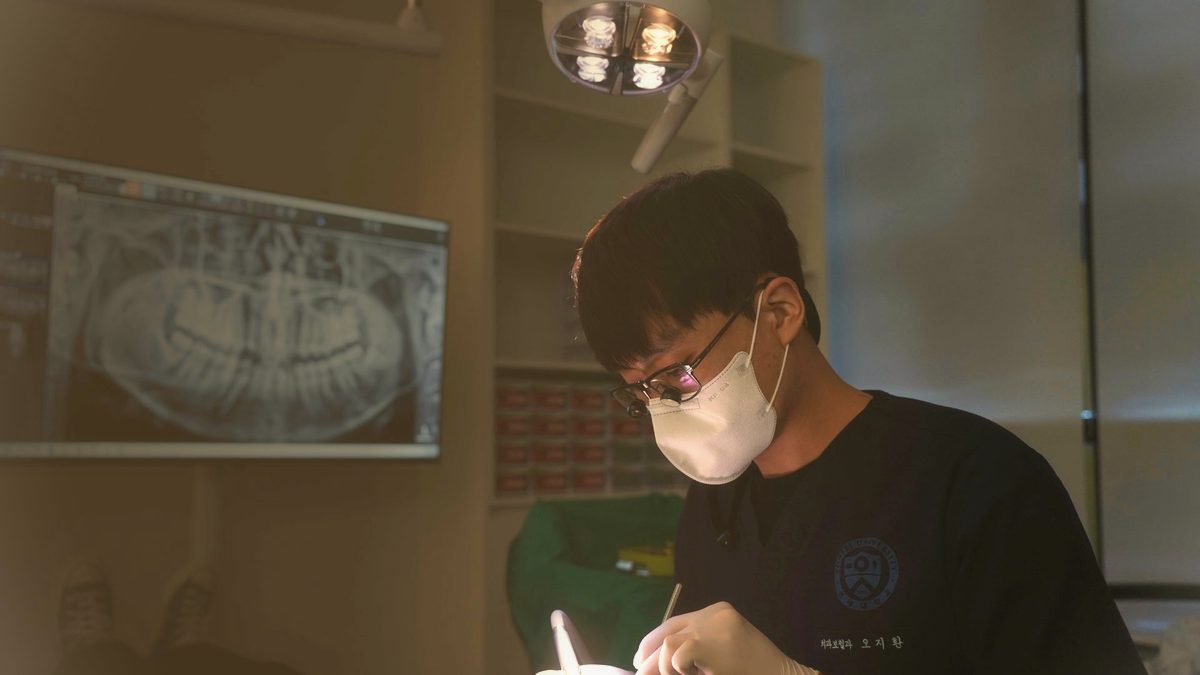 연세더튼튼치과 진료실 모니터에 띄운 치과 파노라마 영상과 진료 중인 원장